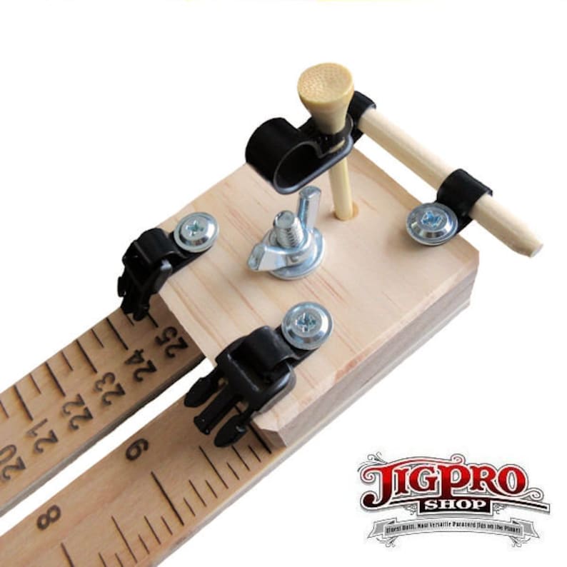 May include: A wooden jig with a ruler, two black clamps, and a golf tee with a wooden dowel attached. The jig is used for woodworking projects.