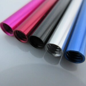 May include: Five metal tubes in different colors: pink, red, black, silver, and blue. The tubes are all the same size and have a threaded end.