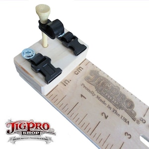 May include: A wooden jig with a ruler marked in inches and centimeters. The jig has two black plastic clamps and a wooden golf tee. The ruler is labeled "JigPro" and "Proudly Made in the USA."