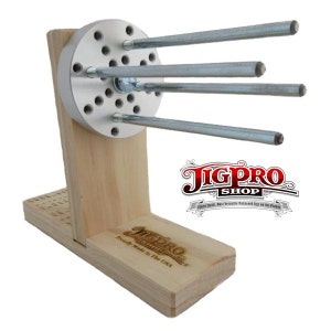 Op de afbeelding: Een houten jig met een metalen basis en meerdere metalen staven die naar buiten steken. De jig is gelabeld met "JigPro Shop" en "Proudly Made in the USA".