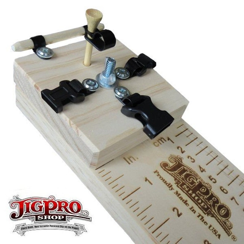 May include: A wooden jig with black clamps and a ruler marked in inches and centimeters. The jig is designed for woodworking projects and features a golf tee and a screw for holding pieces in place. The text "JigPro Shop" is printed on the jig.  Proudly Made in the USA.