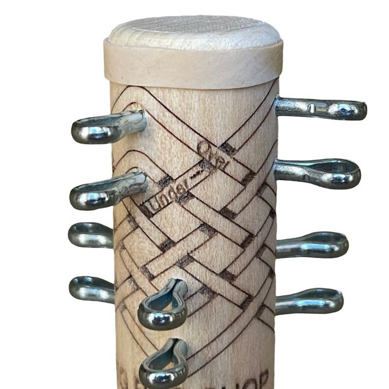 Pu&ograve; includere: Una scatola di legno con un design intrecciato e le parole "Under Over" incise sul lato. La scatola ha sei anelli di metallo sul lato.