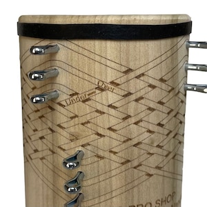 Pu&ograve; includere: Uno strumento in legno con una fascia in pelle nera e ganci in metallo. Lo strumento presenta un motivo intrecciato con le parole "Under" e "Over" incise su di esso. Lo strumento &egrave; etichettato "Pro Shop"