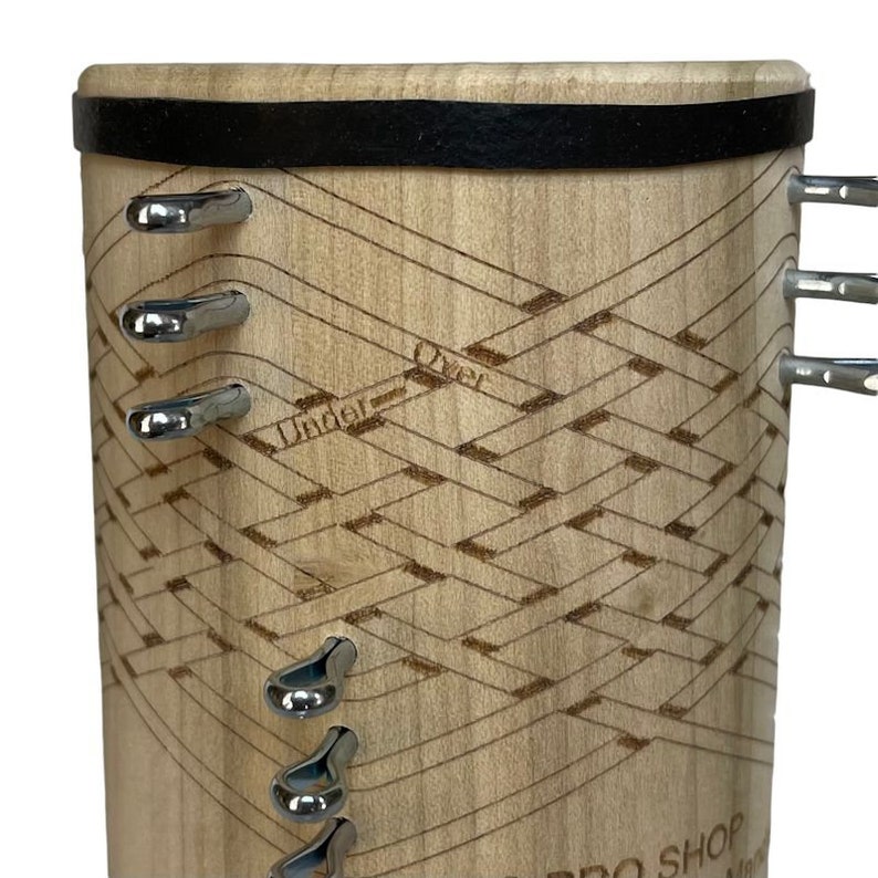 Pu&ograve; includere: Uno strumento in legno con una fascia in pelle nera e ganci in metallo. Lo strumento presenta un motivo intrecciato con le parole "Under" e "Over" incise su di esso. Lo strumento &egrave; etichettato "Pro Shop"