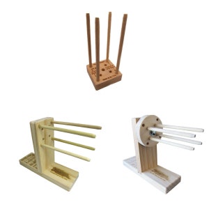 May include: Three wooden dowel rod holders. The first holder is a square base with four dowel rods standing upright. The second holder is a vertical stand with three dowel rods. The third holder is a vertical stand with a round base and three dowel rods.