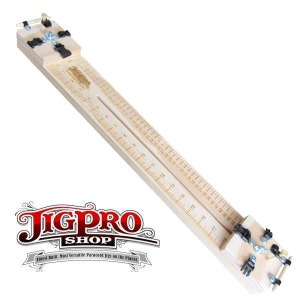 May include: A wooden jig with a ruler marked in inches, used for making paracord bracelets. The jig has a clamping mechanism at each end and a center guide for the paracord. The jig is labeled "JigPro Shop" and "Finest Built, Most Versatile Paracord Jigs on the Planet".