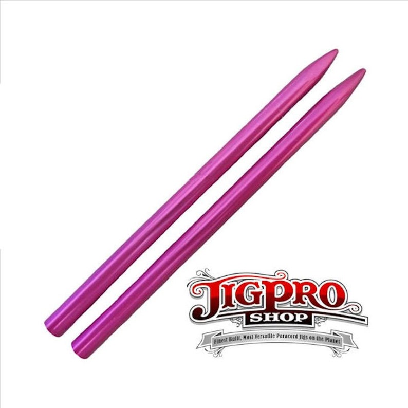 May include: Two pink knitting needles, approximately 10 inches long, with pointed tips. The needles are made of metal and have a smooth, shiny finish. The needles are arranged in a parallel position, with the tips pointing in the same direction.