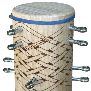 Pu&ograve; includere: Un cilindro di legno con un elastico blu attorno alla parte superiore. Il cilindro presenta un motivo intrecciato con le parole "Under" e "Over" scritte su di esso. Otto ganci metallici sono attaccati al cilindro.