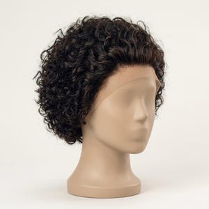 May include: A short, dark brown wig with tight, defined curls styled in a voluminous, rounded shape. The wig features a sheer lace front hairline that sits against the forehead of a smooth, featureless mannequin head with a neutral tone.