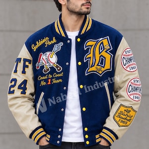 Puede incluir: Una chaqueta universitaria azul marino con mangas beige, ribetes a rayas amarillas y blancas, y botones a presión amarillos. Incluye parches bordados con un gráfico de béisbol y el texto Goldiein Park, Coast to Coast No. 1 Team y State Champion 1969.