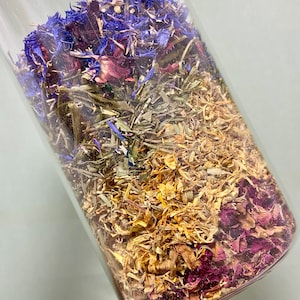 Peut inclure: Un bocal en verre rempli d'un mélange d'herbes et de fleurs séchées. Les herbes sont un mélange de brun clair, jaune et vert, tandis que les fleurs sont violettes, bleues et blanches.