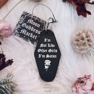 May include: Black motel key chain with a white rose and the text "I'm Not Like Other Girls I'm Satan".
