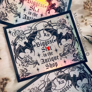 May include: Several rectangular stickers with black borders and a bat and floral design. The text "Biggest Slut in the Antique Shop" is displayed on the stickers. The stickers have a holographic effect.