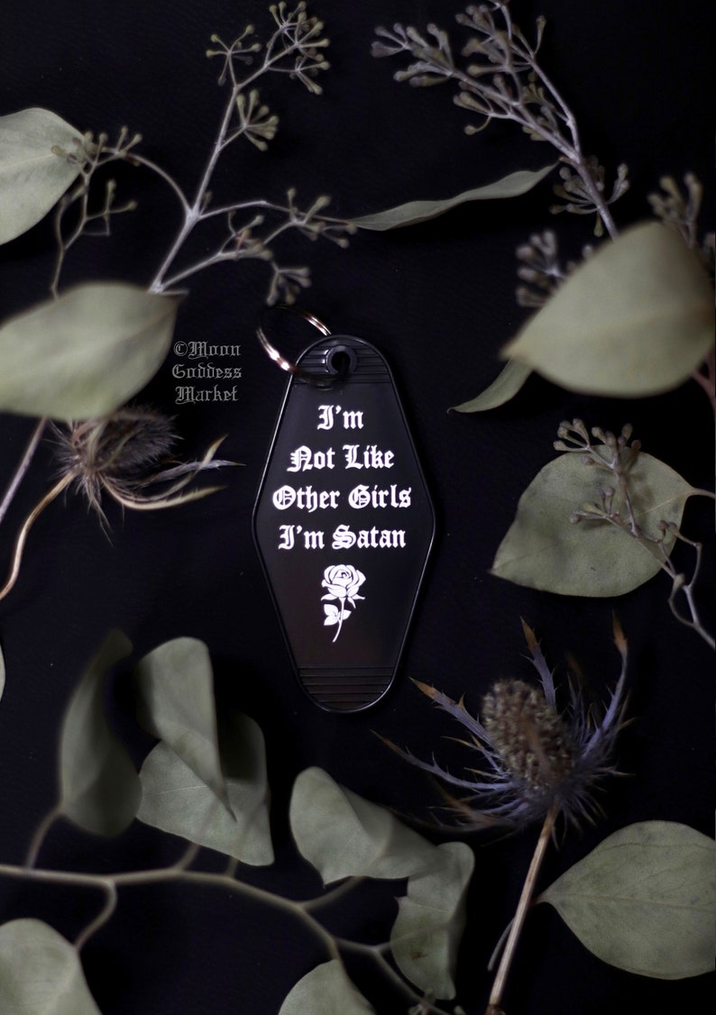 May include: Black metal keychain with a white rose and the text "I'm Not Like Other Girls I'm Satan".