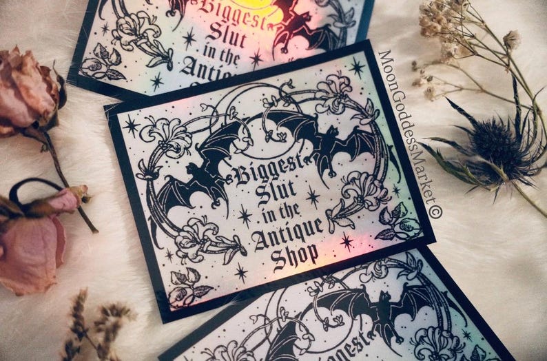 May include: Rectangular stickers with a black border and the text "Biggest Slut in the Antique Shop". The stickers feature a design of bats, flowers, and a crescent moon. The background has a holographic effect.