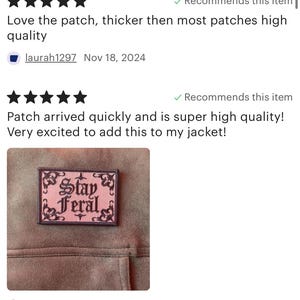 May include: A pink and black embroidered iron-on patch with the text "Stay Feral" in a gothic font. The patch is sewn onto a brown fabric jacket.