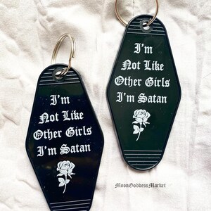 May include: Two black motel keychains with white text that reads "I'm Not Like Other Girls I'm Satan" and a white rose graphic.