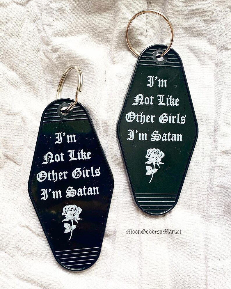 May include: Two black motel keychains with white text that reads "I'm Not Like Other Girls I'm Satan" and a white rose graphic.