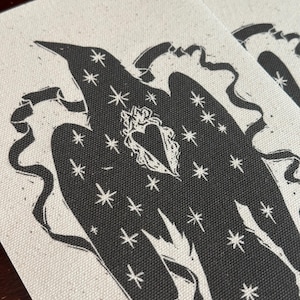 Peut inclure: Une pièce de toile rectangulaire blanc cassé avec une impression sérigraphiée noire représentant un oiseau. L'oiseau est orné de motifs d'étoiles blanches et présente un emblème de cœur central sur la poitrine, entouré d'une bordure en ruban.
