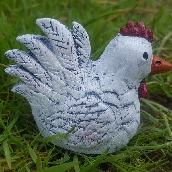 May include: White ceramic chicken figurine with a red comb and beak, sitting on a bed of green grass.