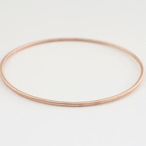 May include: A simple, rose gold bangle bracelet. The bracelet is made of a thin, smooth metal and has a polished finish.