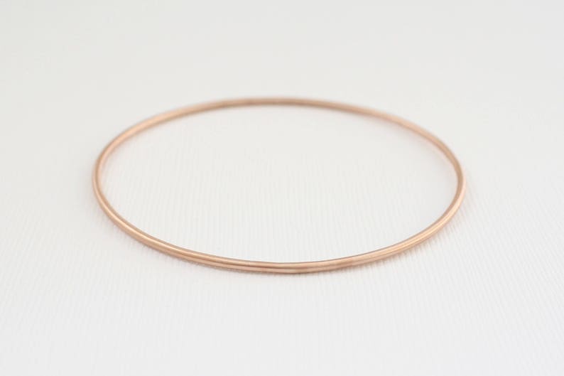 May include: A simple, rose gold bangle bracelet. The bracelet is made of a thin, smooth metal and has a polished finish.