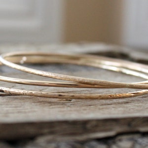 May include: Three gold bangles stacked on top of each other. The bangles are hammered and have a textured surface.