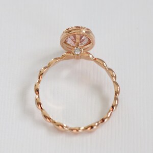 May include: A rose gold ring with a pink gemstone set in a bezel setting. The band is twisted and has a delicate design.
