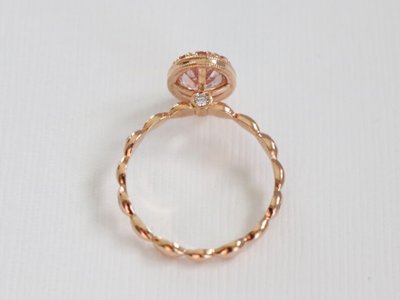 May include: A rose gold ring with a pink gemstone set in a bezel setting. The band is twisted and has a delicate design.