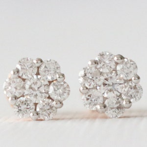 May include: A pair of small, round, silver stud earrings with a cluster of clear diamonds.