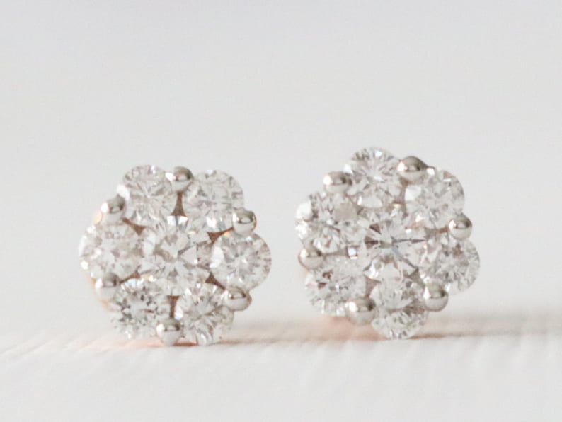May include: A pair of small, round, silver stud earrings with a cluster of clear diamonds.