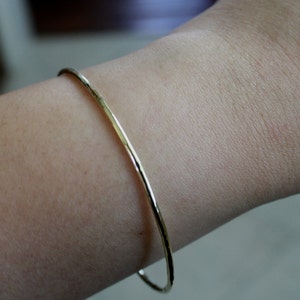 May include: A simple gold bangle bracelet with a hammered finish.