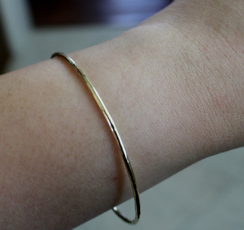 May include: A simple gold bangle bracelet with a hammered finish.