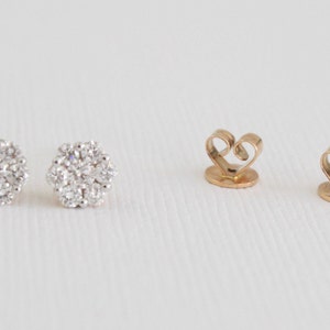 May include: A pair of gold earrings with a cluster of small, clear diamonds. The earrings have a heart-shaped back.