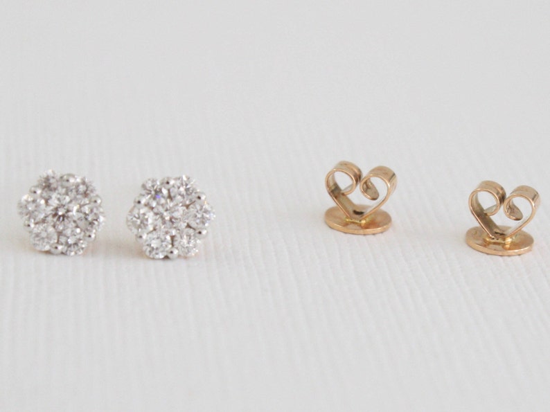 May include: A pair of gold earrings with a cluster of small, clear diamonds. The earrings have a heart-shaped back.