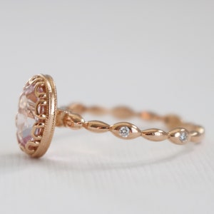 May include: A rose gold ring with a large oval-shaped pink gemstone set in a delicate filigree design. The band is adorned with small round diamonds set in a scalloped pattern.
