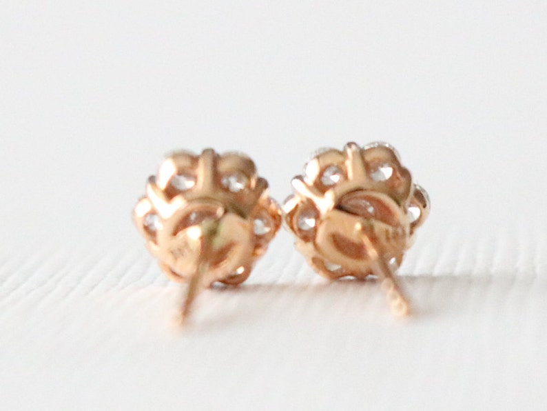 May include: A pair of rose gold stud earrings with a cluster of small clear stones.