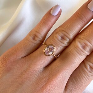 May include: A delicate gold ring with a pink oval-shaped gemstone set in a detailed filigree design.