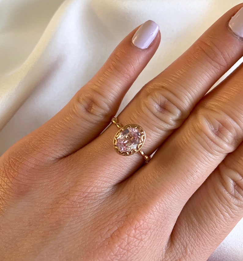 May include: A delicate gold ring with a pink oval-shaped gemstone set in a detailed filigree design.