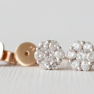 May include: A pair of small, round diamond earrings with a cluster of small diamonds set in a flower shape. The earrings are made of gold and have a white gold setting.