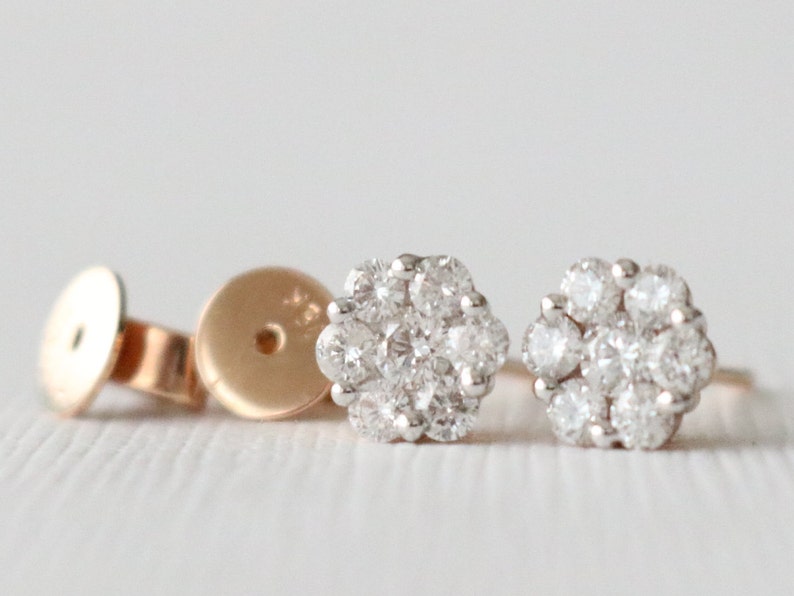 May include: A pair of small, round diamond earrings with a cluster of small diamonds set in a flower shape. The earrings are made of gold and have a white gold setting.