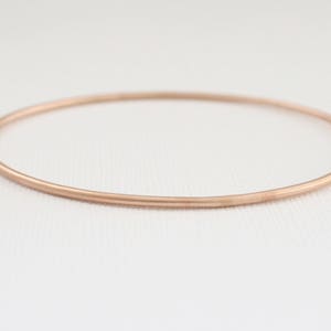 May include: A simple, rose gold bangle bracelet. The bracelet is thin and has a smooth, polished finish.
