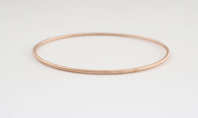 May include: A simple, rose gold bangle bracelet. The bracelet is thin and has a smooth, polished finish.