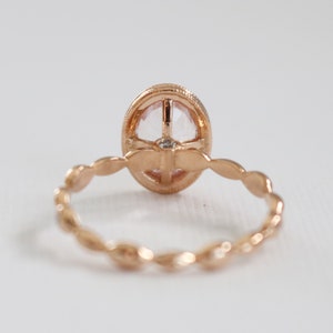 May include: A rose gold ring with a delicate, oval-shaped gemstone set in a bezel setting. The band is adorned with a delicate, twisted design.