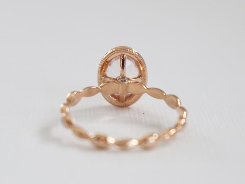 May include: A rose gold ring with a delicate, oval-shaped gemstone set in a bezel setting. The band is adorned with a delicate, twisted design.