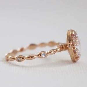 May include: A rose gold ring with a large oval-shaped gemstone surrounded by smaller gemstones. The band is a delicate, twisted design with small gemstones set into the band.