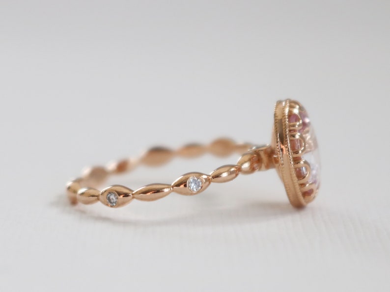 May include: A rose gold ring with a large oval-shaped gemstone surrounded by smaller gemstones. The band is a delicate, twisted design with small gemstones set into the band.