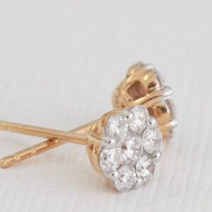 May include: A pair of gold stud earrings with a cluster of small, clear diamonds in a flower shape.