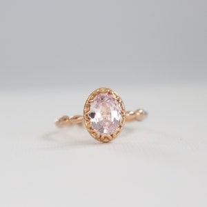 May include: A delicate rose gold ring with a pink oval gemstone set in a detailed filigree design.