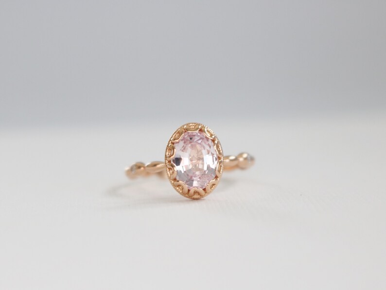 May include: A delicate rose gold ring with a pink oval gemstone set in a detailed filigree design.